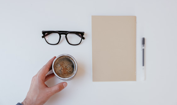 Coffee cup, glasses, notebook and pen on a desk